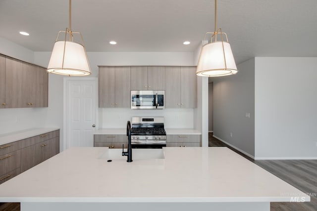 kitchen featuring light countertops, appliances with stainless steel finishes, an island with sink, and decorative light fixtures