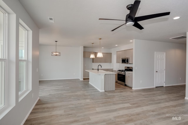 kitchen featuring decorative light fixtures, a center island with sink, stainless steel appliances, light countertops, and open floor plan