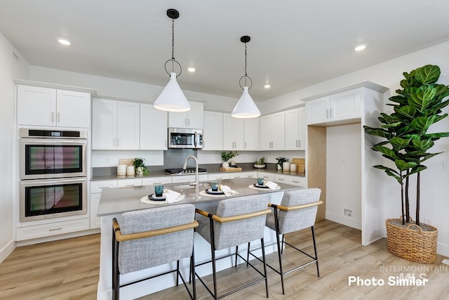 kitchen with white cabinets, stainless steel appliances, a kitchen island with sink, and light hardwood / wood-style flooring