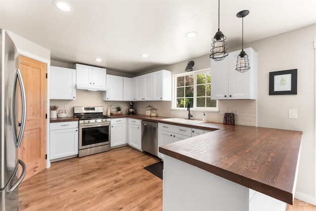 kitchen featuring stainless steel appliances, dark countertops, a sink, a peninsula, and tasteful backsplash