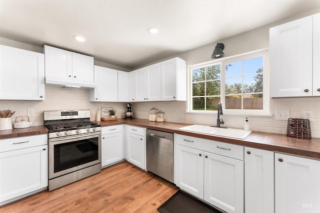 kitchen featuring stainless steel appliances, a sink, butcher block countertops, under cabinet range hood, and backsplash
