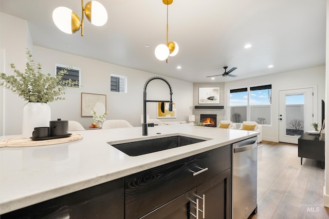 kitchen with light wood-type flooring, pendant lighting, a sink, stainless steel dishwasher, and a large fireplace