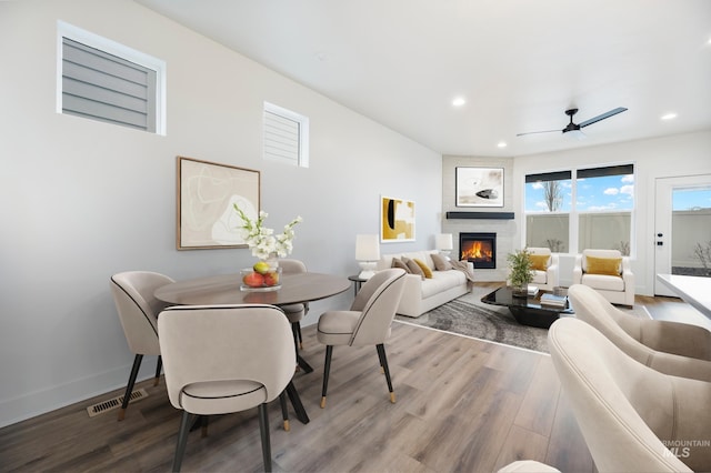 dining area with a ceiling fan, wood finished floors, recessed lighting, a large fireplace, and baseboards