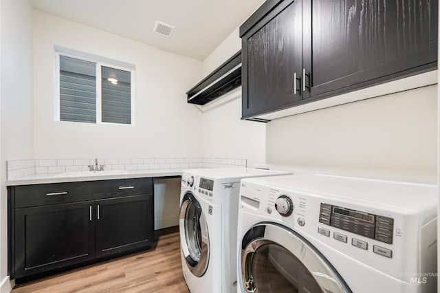 laundry area with visible vents, a sink, cabinet space, light wood-style floors, and washing machine and clothes dryer