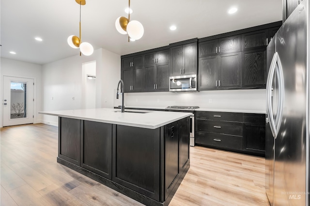 kitchen featuring light wood-type flooring, a sink, dark cabinetry, stainless steel appliances, and light countertops