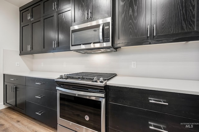 kitchen featuring light countertops, light wood-style flooring, dark cabinets, and appliances with stainless steel finishes