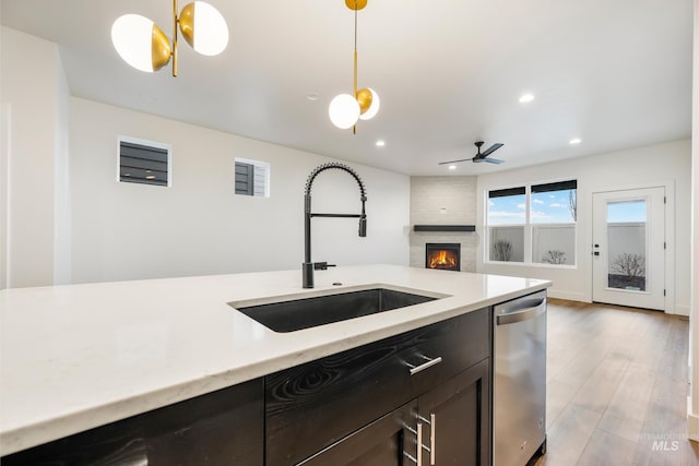 kitchen with a large fireplace, pendant lighting, stainless steel dishwasher, wood finished floors, and a sink