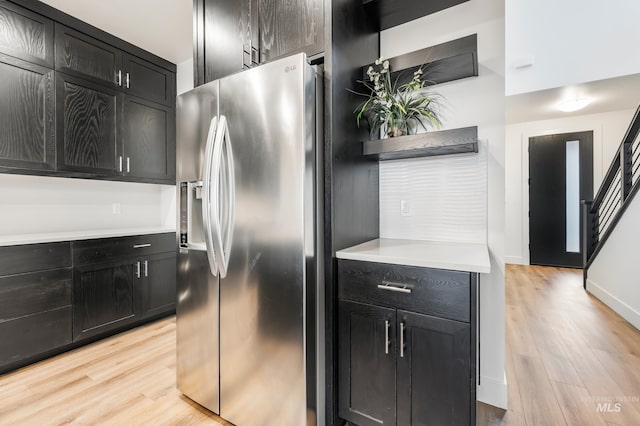 kitchen with light wood-style flooring, dark cabinetry, stainless steel refrigerator with ice dispenser, and light countertops