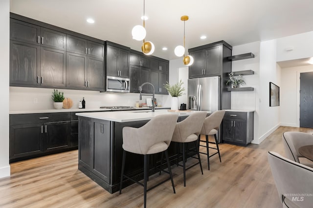 kitchen with light wood finished floors, open shelves, stainless steel appliances, light countertops, and a kitchen bar