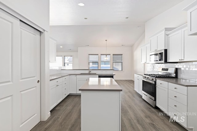 kitchen featuring appliances with stainless steel finishes, a kitchen island, white cabinetry, dark hardwood / wood-style flooring, and vaulted ceiling