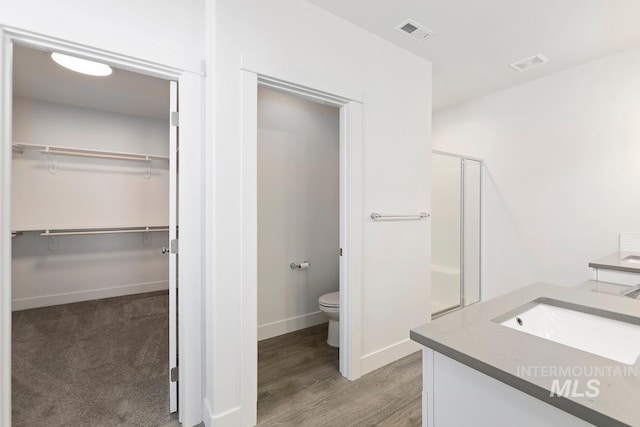 bathroom featuring toilet, vanity, a shower with door, and hardwood / wood-style floors