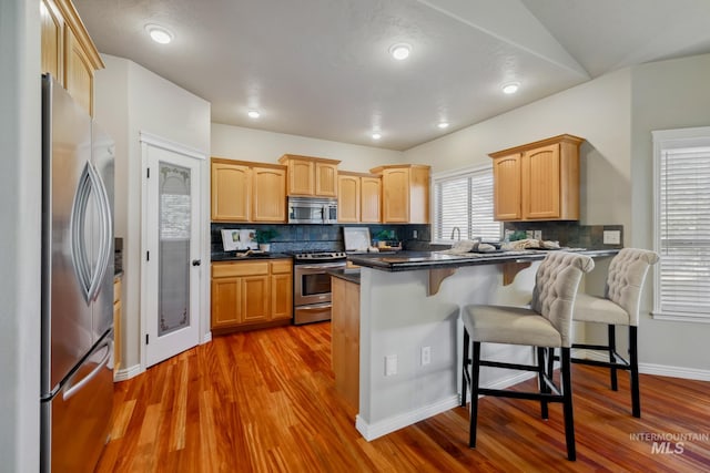 kitchen with stainless steel appliances, backsplash, kitchen peninsula, hardwood / wood-style flooring, and a breakfast bar