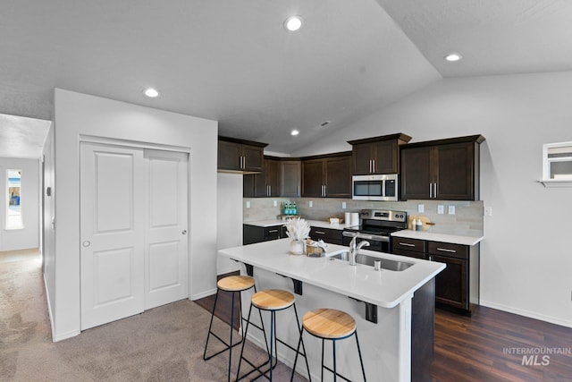 kitchen with a breakfast bar, a kitchen island with sink, sink, vaulted ceiling, and stainless steel appliances