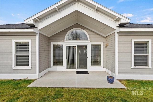 view of exterior entry with a lawn and a patio