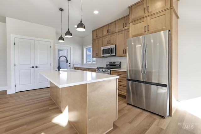 kitchen featuring sink, a center island with sink, light wood-type flooring, appliances with stainless steel finishes, and pendant lighting