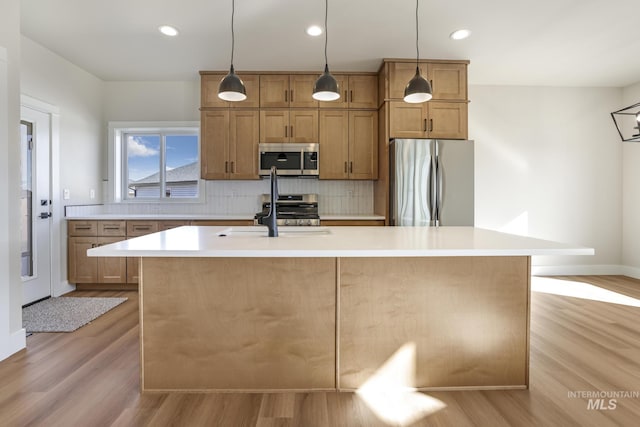 kitchen with sink, appliances with stainless steel finishes, a kitchen island with sink, light hardwood / wood-style floors, and backsplash