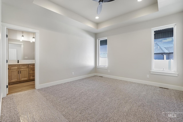 unfurnished bedroom featuring light carpet, a tray ceiling, ceiling fan, and ensuite bathroom