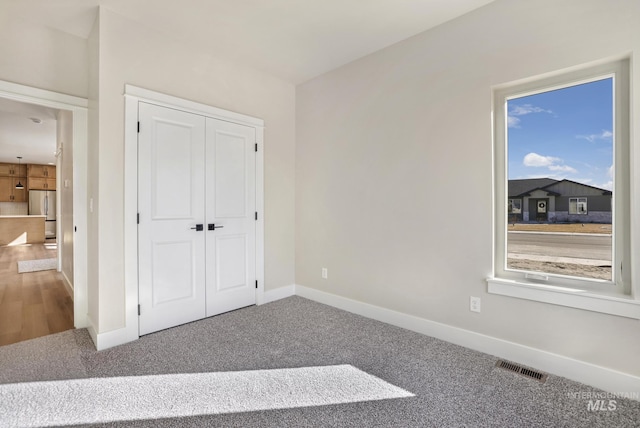 unfurnished bedroom featuring carpet flooring, stainless steel fridge, and a closet