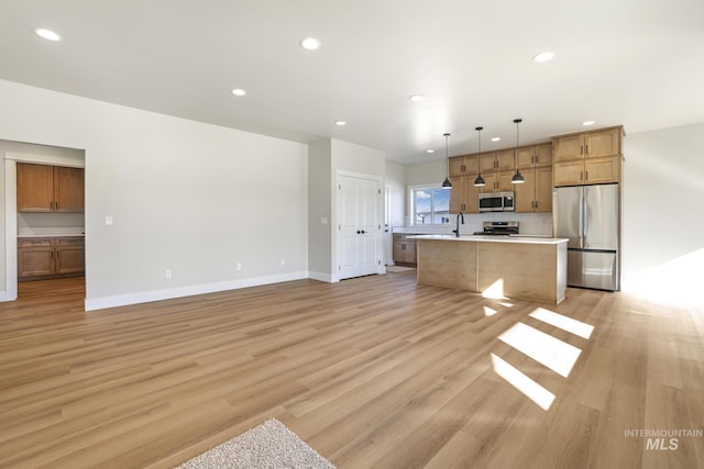 kitchen featuring pendant lighting, light hardwood / wood-style flooring, stainless steel appliances, a kitchen island, and decorative backsplash