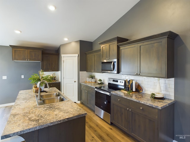 kitchen featuring sink, lofted ceiling, light hardwood / wood-style floors, an island with sink, and appliances with stainless steel finishes