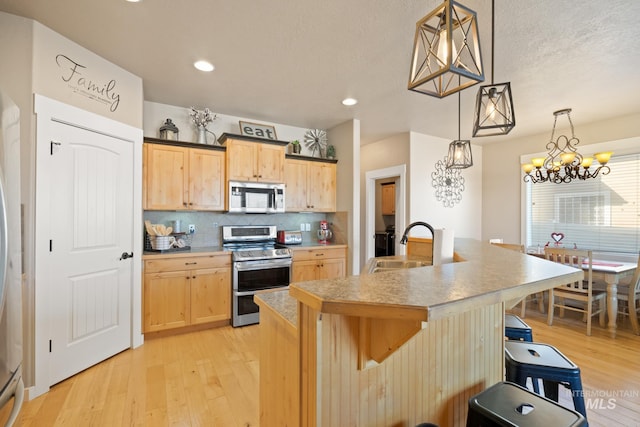 kitchen with stainless steel appliances, tasteful backsplash, light brown cabinetry, and decorative light fixtures