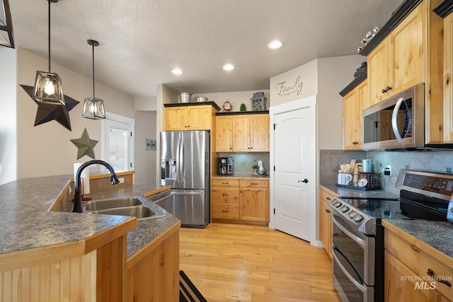 kitchen featuring pendant lighting, sink, backsplash, stainless steel appliances, and light wood-type flooring