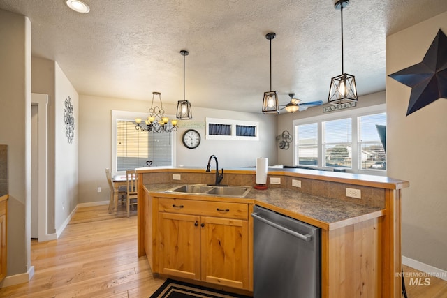 kitchen featuring pendant lighting, sink, light wood-type flooring, stainless steel dishwasher, and a textured ceiling