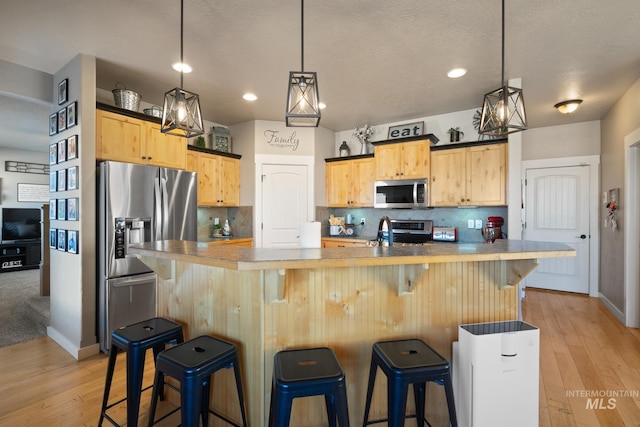 kitchen featuring light brown cabinetry, decorative backsplash, stainless steel appliances, and light wood-type flooring