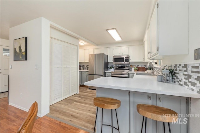 kitchen featuring sink, appliances with stainless steel finishes, white cabinetry, a kitchen bar, and kitchen peninsula