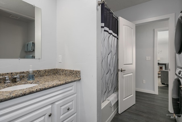 bathroom featuring baseboards, wood finished floors, vanity, shower / tub combo, and stacked washing maching and dryer