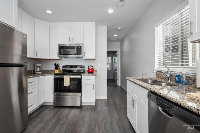 kitchen featuring dark wood finished floors, a sink, light stone counters, white cabinets, and appliances with stainless steel finishes
