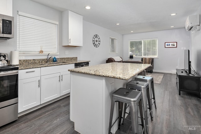 kitchen with a kitchen breakfast bar, a wall unit AC, dark wood-style flooring, a sink, and appliances with stainless steel finishes