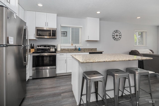 kitchen with a kitchen bar, open floor plan, stainless steel appliances, white cabinets, and dark wood-style flooring