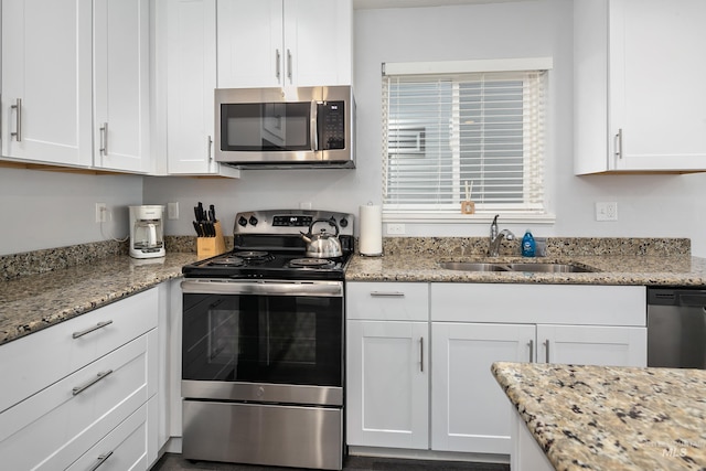kitchen featuring white cabinets, a sink, stainless steel appliances, and light stone countertops
