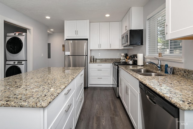 kitchen featuring stacked washer / drying machine, a sink, appliances with stainless steel finishes, white cabinets, and dark wood-style flooring