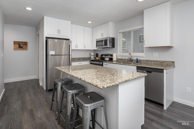 kitchen featuring a sink, white cabinetry, a breakfast bar, appliances with stainless steel finishes, and dark wood-style flooring