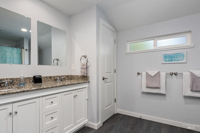 bathroom featuring baseboards, wood finished floors, double vanity, and a sink