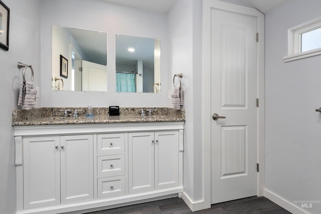 full bath featuring a shower with curtain, baseboards, a sink, double vanity, and wood finished floors