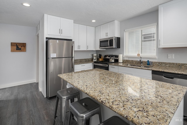 kitchen with a sink, light stone countertops, appliances with stainless steel finishes, and white cabinets