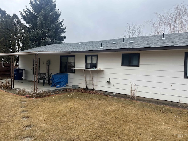 rear view of property with a yard, roof with shingles, and a patio