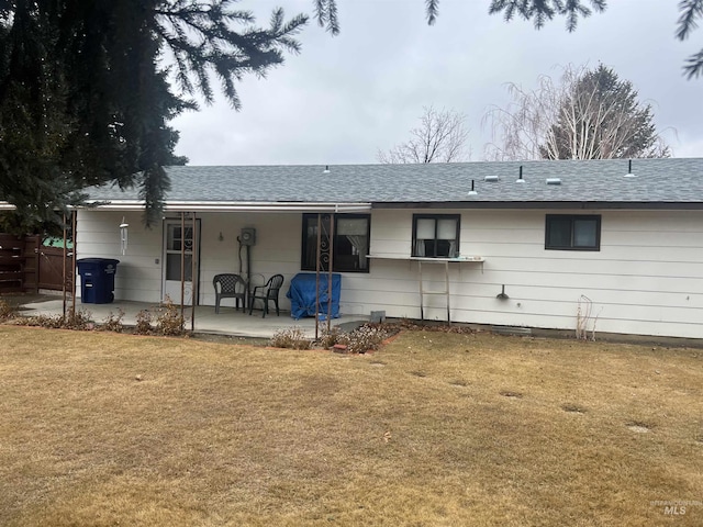 back of property with roof with shingles, fence, a lawn, and a patio