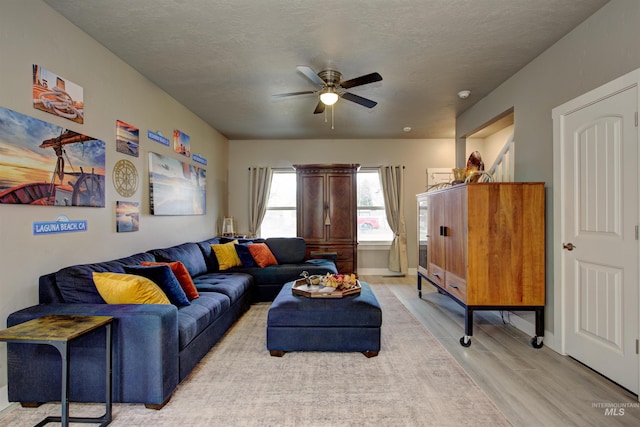 living room featuring ceiling fan, light hardwood / wood-style flooring, and a textured ceiling