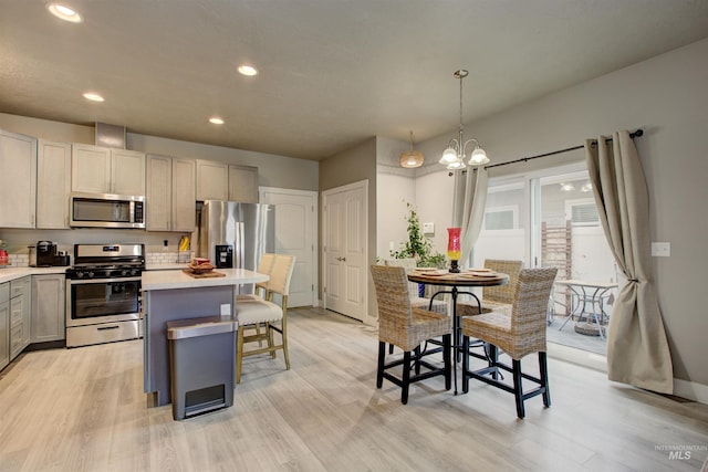 kitchen with gray cabinetry, hanging light fixtures, a center island, light hardwood / wood-style floors, and stainless steel appliances