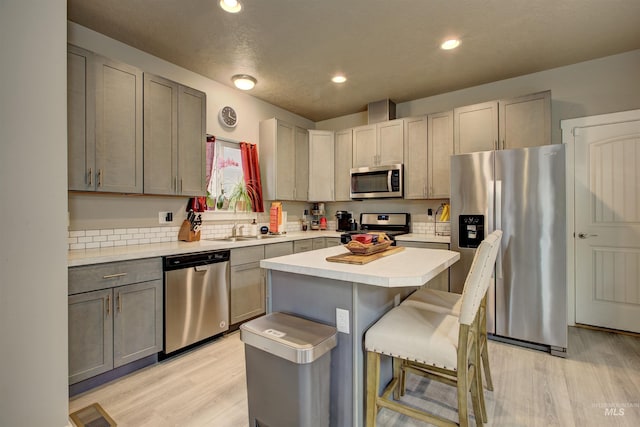 kitchen with a kitchen bar, sink, gray cabinetry, a center island, and appliances with stainless steel finishes