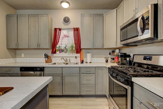 kitchen featuring stainless steel appliances, sink, light wood-type flooring, and gray cabinets