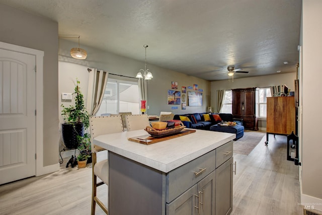 kitchen featuring decorative light fixtures, gray cabinets, a breakfast bar area, and light hardwood / wood-style flooring