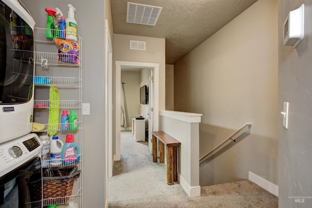 stairs with stacked washer / dryer, carpet flooring, and a textured ceiling