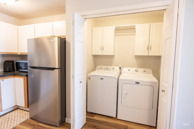 washroom featuring cabinet space, wood finished floors, and washer and clothes dryer