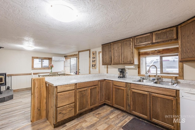 kitchen with a wall mounted AC, a peninsula, white dishwasher, a sink, and light wood-style floors