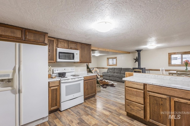 kitchen featuring open floor plan, a wood stove, wood finished floors, brown cabinetry, and white appliances